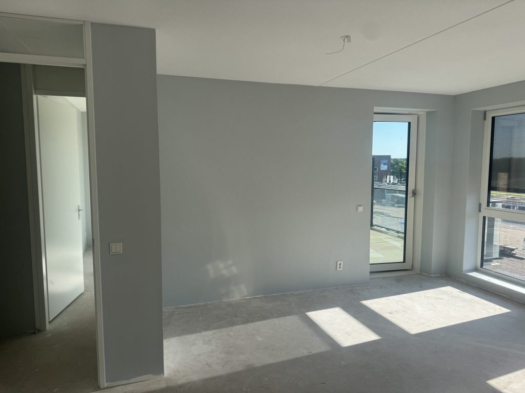 Lege kamer van een pas opgeleverde woning met kale wanden en een betonvloer