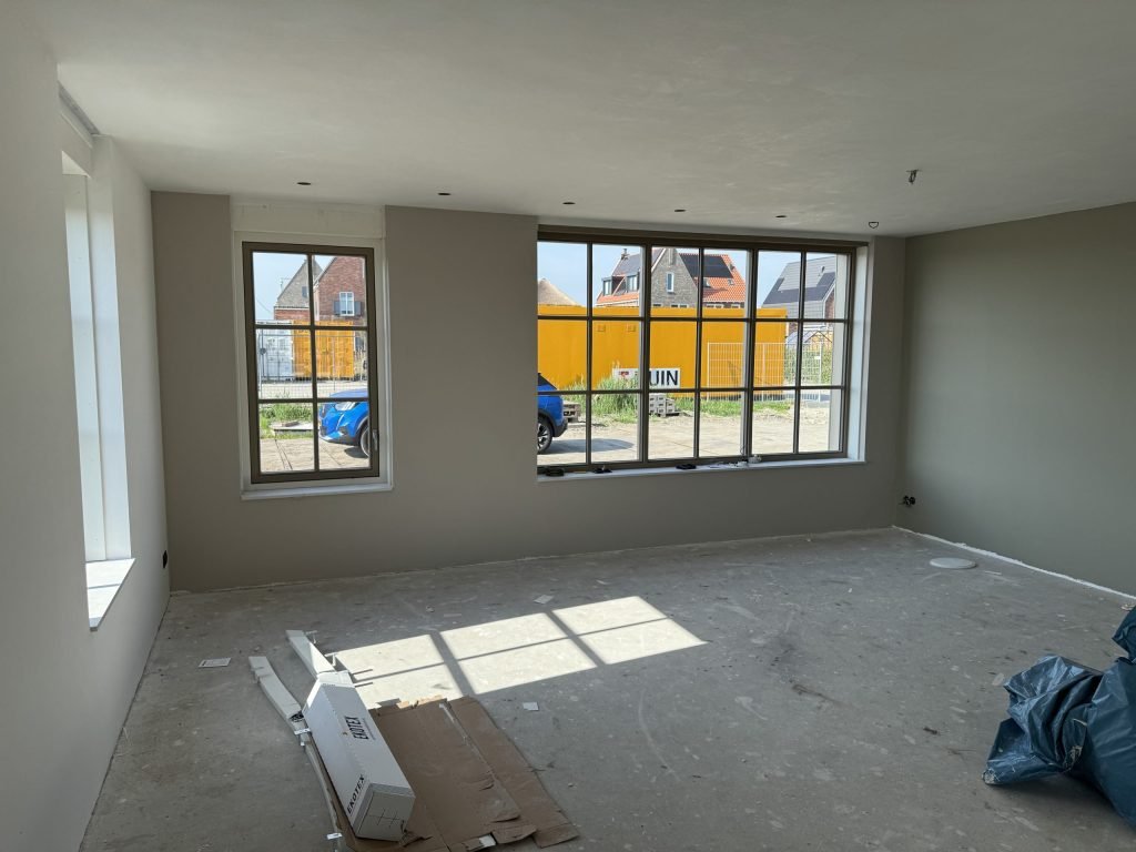 Woonkamer met afgewerkte grijsgroene wanden en een grote roedenpui