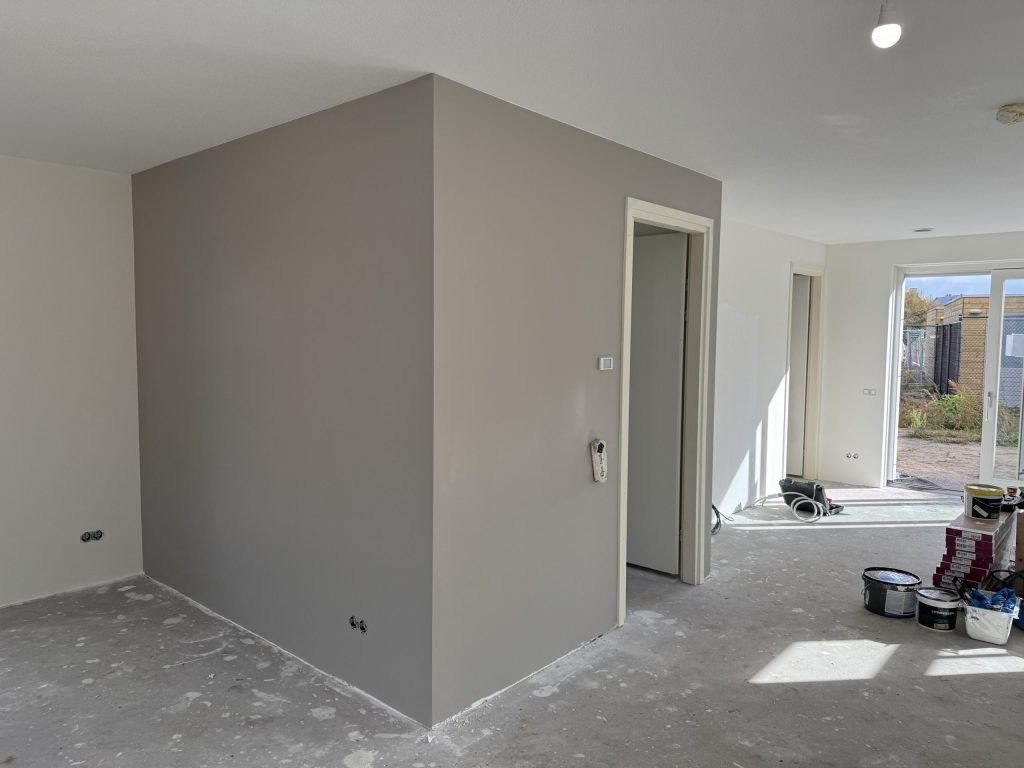 Woning waarin net een wand is afgewerkt, met verfemmers op de vloer