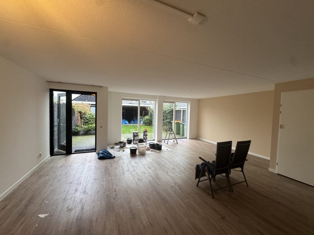 Lichte woonkamer met tuindeuren en verfemmers op de vloer tijdens het afwerken van de wanden